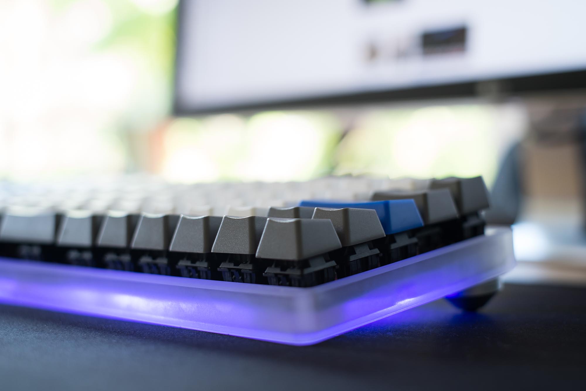 Front angle view of keyboard with acrylic case and purple glowing LEDs