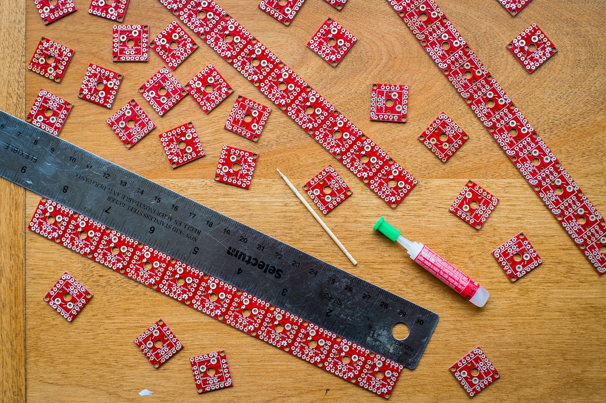 Tiny individual key PCB&#39;s scattered on a desk with ruler to make them straight and glue to connect them