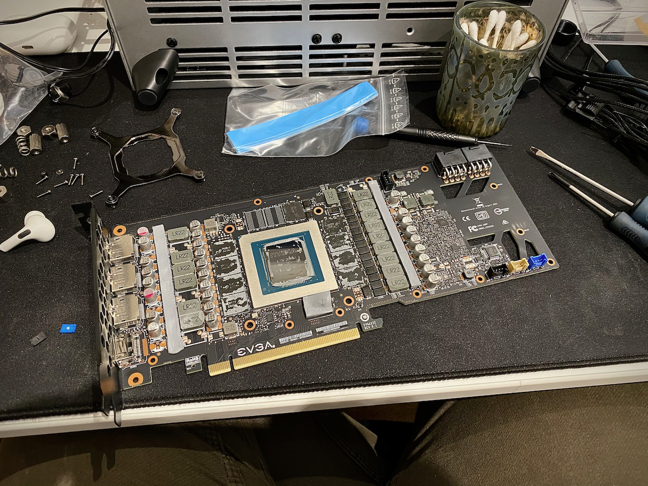 The graphics card with no cooler on. The components are all visible and there is still grey thermal paste coating some of the components. The desk is in disarray around the card.